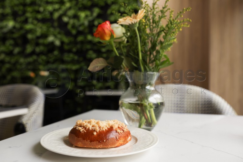 Tasty bun and vase with flowers on table in cafeteria