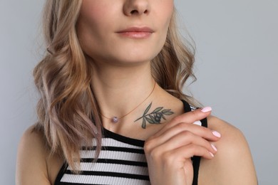 Beautiful woman with tattoo on body against grey background, closeup
