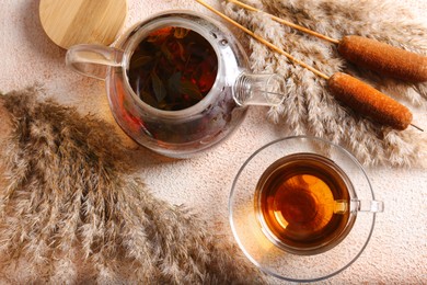 Photo of Hot tea and beautiful dry reed on beige textured table, flat lay