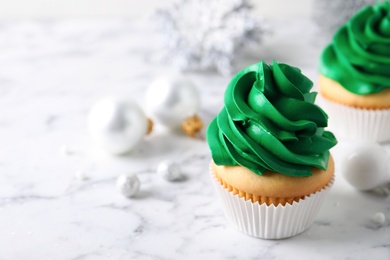 Delicious cupcakes with green cream and Christmas decor on white marble table. Space for text