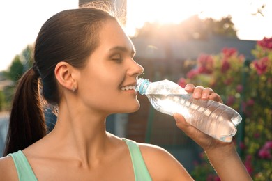 Happy young woman drinking water outdoors on hot summer day. Refreshing drink