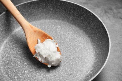 Frying pan with coconut oil on grey background, closeup