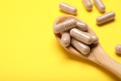 Gelatin capsules in spoon on yellow background, closeup. Space for text