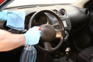 Man cleaning car salon with disinfectant spray and cloth, closeup