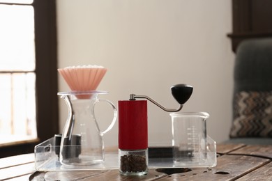 Photo of Manual coffee grinder with beans, glass jug and wave dripper on wooden table in cafe