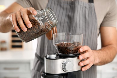 Man using electric coffee grinder in kitchen, closeup