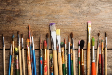Different paint brushes on wooden background, top view with space for text