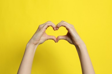 Woman making heart with her hands on yellow background, closeup