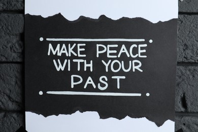 Photo of Card with life-affirming phrase Make Peace With Your Past on dark brick wall, closeup