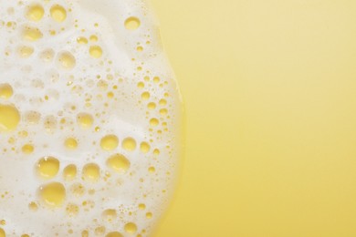 White washing foam on yellow background, top view. Space for text