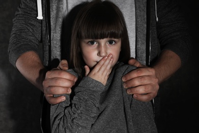 Scared little girl and adult man on dark background. Child in danger