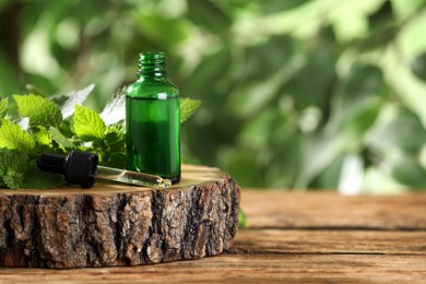 Glass bottle of nettle oil with dropper and fresh leaves on wooden table against blurred background, space for text