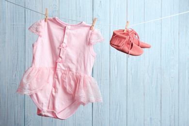 Pair of shoes and bodysuit on laundry line against wooden background. Baby accessories