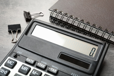 Calculator, notebook and paper clips on grey table, closeup. Tax accounting