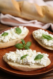 Photo of Bread with cottage cheese and basil on wooden plate, closeup
