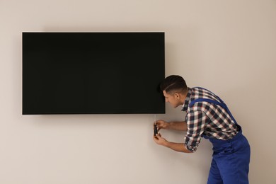 Photo of Professional technician with screwdriver installing modern flat screen TV on wall indoors