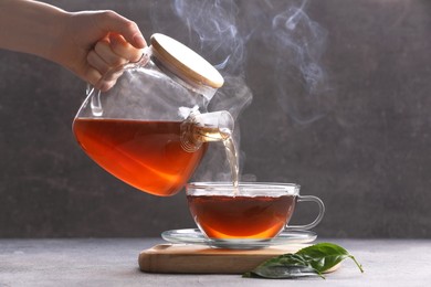 Photo of Woman pouring aromatic hot tea into glass cup on light grey table, closeup