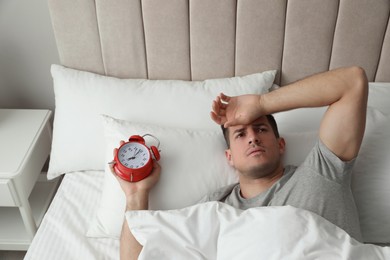 Man with alarm clock in bed. Being late because of oversleeping