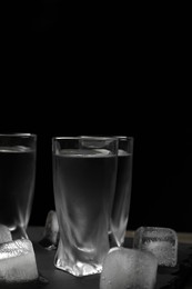 Shot glasses of vodka with ice cubes on table against black background