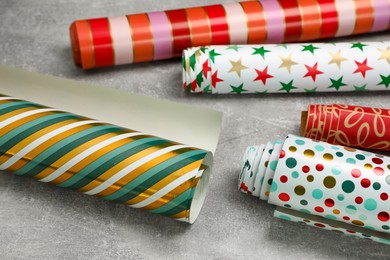 Different colorful wrapping paper rolls on grey table, closeup
