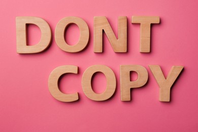 Photo of Words Don't Copy made of wooden letters on dark pink background, flat lay. Plagiarism concept