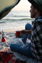 Man with cup of hot drink in camping tent