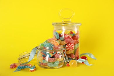 Jars with different delicious candies on yellow background