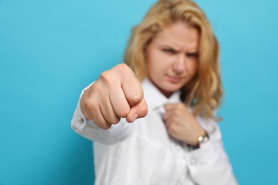 Young woman ready to fight against light blue background, focus on fist
