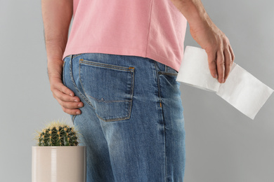 Man with toilet paper sitting down on cactus against light grey background, closeup. Hemorrhoid concept