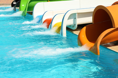Different colorful slides and swimming pool in water park on sunny day