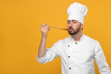 Photo of Mature male chef with spoon tasting dish on orange background, space for text