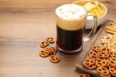Glass of beer served with delicious pretzel crackers and other snacks on wooden table, space for text