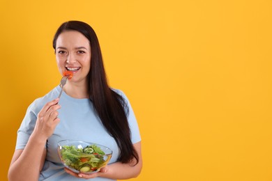 Beautiful overweight woman eating salad on yellow background, space for text. Healthy diet