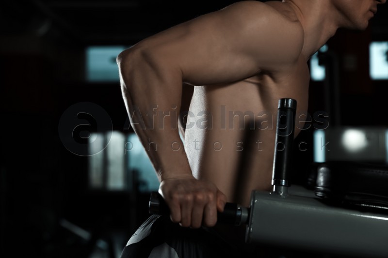 Strong man working out on parallel bars in modern gym, closeup