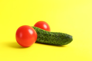 Cucumber and tomatoes symbolizing male genitals on yellow background. Potency concept