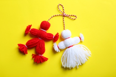 Photo of Traditional martisor shaped as man and woman on yellow background, top view. Beginning of spring celebration
