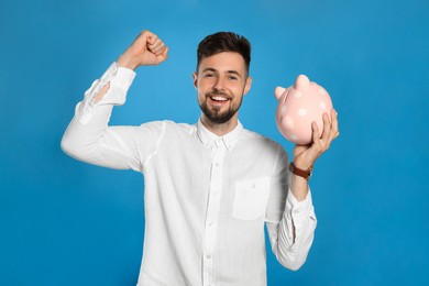 Photo of Happy young man with piggy bank on light blue background