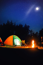 Glowing camping tent near bonfire in wilderness at night