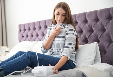 Young woman with asthma machine on bed in light room