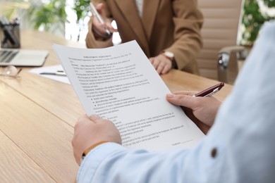 Photo of Man reading employment agreement at table in office, closeup. Signing contract