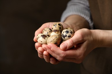 Woman with handful of quail eggs on dark background, closeup