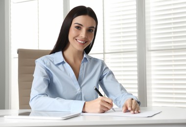 Young businesswoman writing at table in office