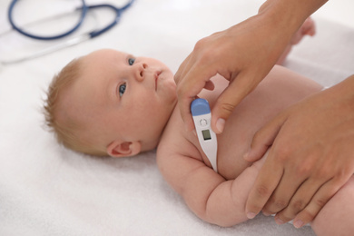 Doctor measuring temperature of little baby with digital thermometer indoors, closeup. Health care