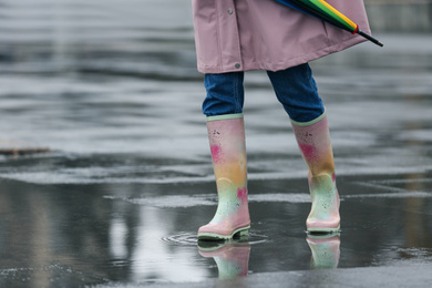 Woman in rubber boots walking outdoors on rainy day, closeup. Space for text