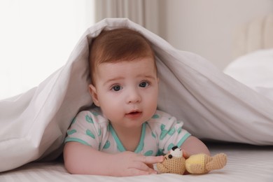 Cute little baby with toy in bed under soft blanket indoors
