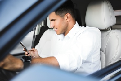 Handsome man using smartphone while driving his modern car