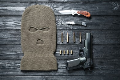 Photo of Flat lay composition with balaclava and weapons on black wooden table
