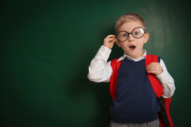 Funny little child wearing glasses near chalkboard, space for text. First time at school