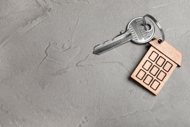 Key with trinket in shape of house on grey stone background, top view and space for text. Real estate agent services