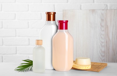 Photo of Different bottles of shampoo and green leaf on white table